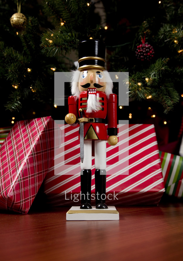 a nutcracker in front of Christmas gifts under a Christmas tree 