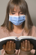 a woman reading a Bible while wearing a face mask 