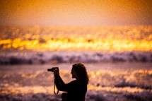 woman taking a picture on a beach at sunset 