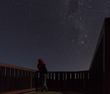 man standing on a balcony looking out at stars 