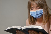 a woman wearing a face mask while reading a Bible 