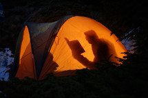 Silhouette Of A Man Reading A Book In A Tent in The Wilderness