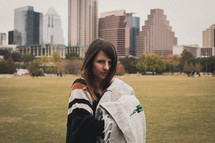 a woman standing in a city park holding a blanket 
