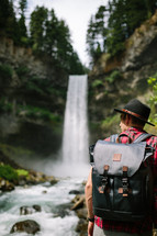 a man with a backpack standing in front of a waterfall 