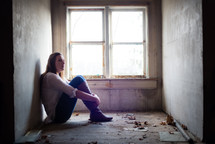 teen girl sitting alone in an empty room near a window 