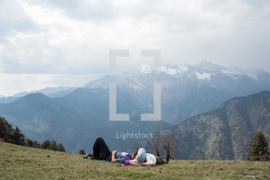 man and woman lying on the ground looking out at snow capped mountains 
