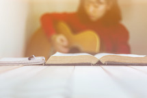 a woman playing a guitar and reading a Bible 