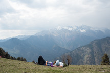 man and woman lying on the ground looking out at snow capped mountains 