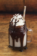 Chocolate Milk Shake Dripping with Chocolate Sauce on a Wooden Table