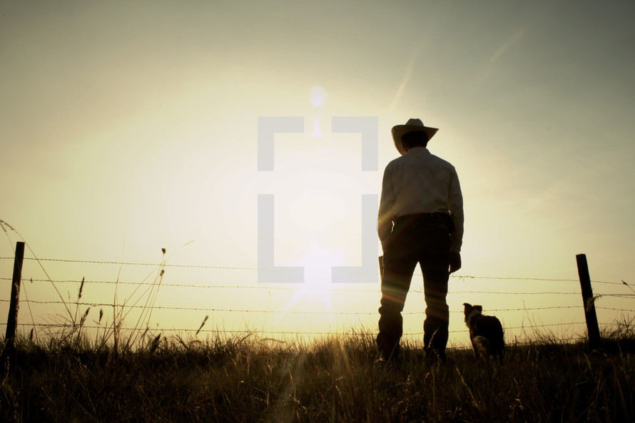 A rancher and his dog in a field at sunset 