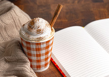 A Pumpkin Spice Latte Topped with Whipped Cream in a Disposable Cup on a Wood Background