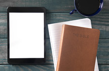 tablet, Bible, notebook, and coffee cup on a green wood background 