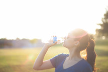 Woman drinking from a water bottle outside.