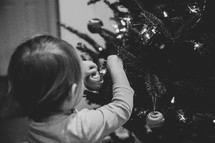 Small child hanging ornaments on a Christmas tree - black and white