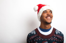 man in an ugly Christmas sweater and santa hat smiling looking up 