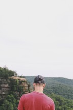 a man in a ball cap looking out at mountains 