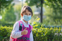 Little school girl going back to school after pandemic outbreak wearing an face mask