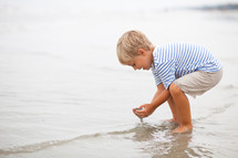 Boy scooping wet sand on the beach.