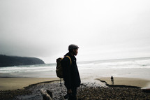 man with a backpack standing on a rocky beach 