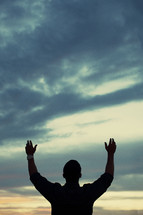 Man standing outside with arms raised in praise.