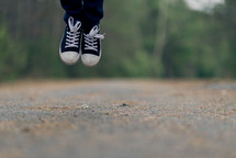 A person's feet jumping above a country road.