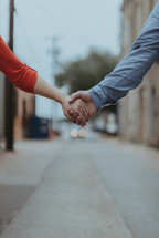 a couple holding hands walking down a street 