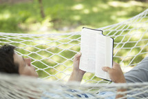 man reading a Bible in a hammock.