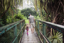 father and daughter holding hands walking across a bridge 