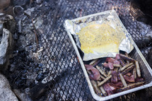 cooking bacon and sausage over a campfire 