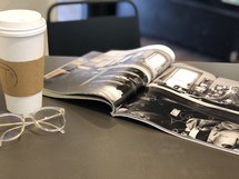 pages of an opened book, reading glasses, and coffee cup on a table 