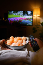 Closeup Woman Eating Tangerine And Watching TV On Bed