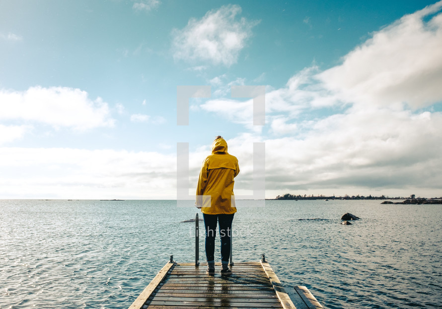a woman in a yellow raincoat standing on a dock in winter 
