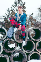 teen boy sitting on concrete pipes in winter snow 