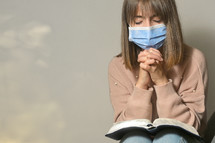 woman wearing a face mask and praying over a Bible in her lap 