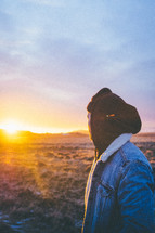a man looking out at the setting sun over a field 