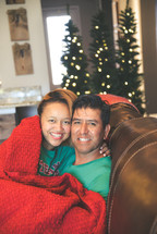 a couple snuggling under a blanket at Christmas 