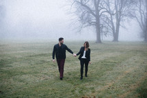 couple holding hands walking in a foggy field 