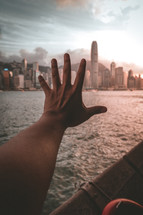hand reaching towards a city over water 