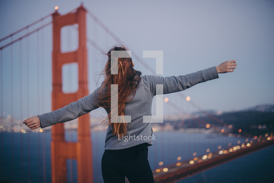a woman with outstretched arms standing in front of the Golden Gate bridge 