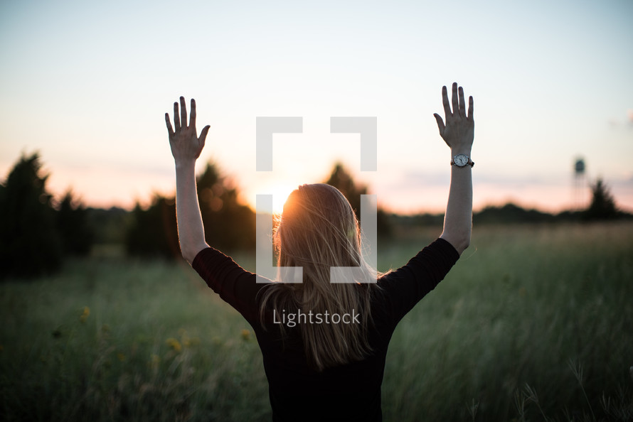 a woman in a field with hands raised to praise God 
