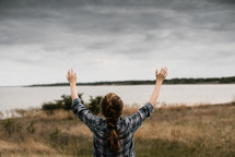 a woman with raised hands standing in front of a lake 