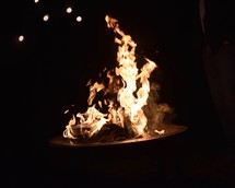 a man standing around glowing flames from a fire pit at night 