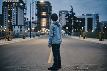 a young boy standing in the middle of a road looking back at a city 