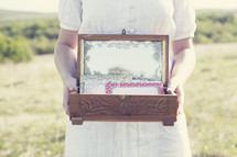 Woman standing in a field of grass holding an antique wooden box of stationery,