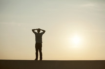 silhouette of a man standing with his hands on his head at sunset.