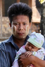 a man holding an infant with traditional face paint 
