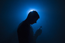 a man praying holding a cross illuminated in darkness 