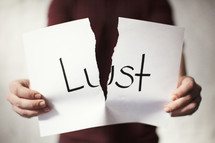 A man tearing apart a piece of paper with the word lust on it 