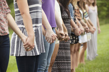 Line of women standing outside holding hands.