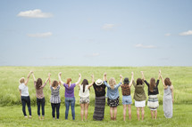Women holding hands with arms raised in praise while standing in a field of grass.